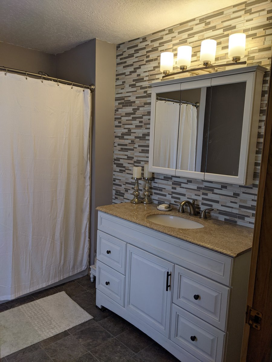 Bathroom with dual-sink white vanity, stone accent wall, and mirror lighting